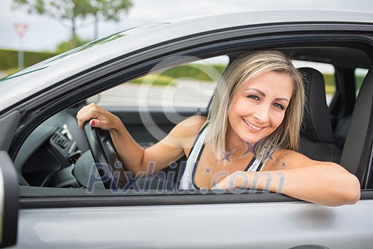 Woman driving a car - female driver at a wheel of a modern car, looking happy, smiling with a relaxed smile (shallow DOF; color toned image) Woman driving a car - female driver at a wheel of a modern car, looking happy, smiling with a relaxed smile (shallow DOF; color toned image)