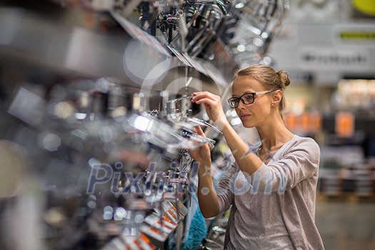 Pretty young woman choosing a bathroom/kitchen tap in a home furnishings retail store Pretty young woman choosing a bathroom/kitchen tap in a home furnishings retail store