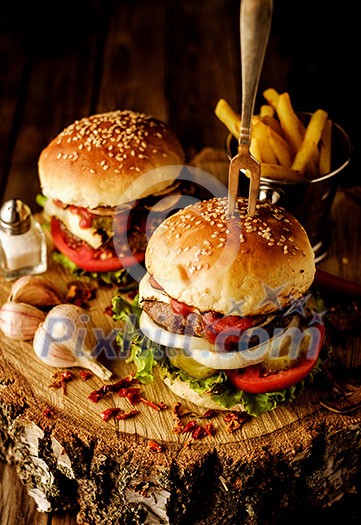 Delicious homemade hamburger with lettuce and cheese. Fried chips and burger on wooden background.