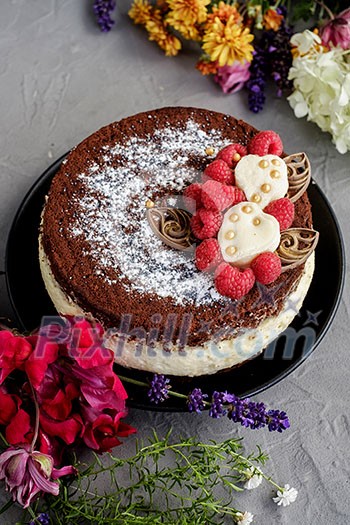 Chocolate raspberry cream cake with flowers on a grey background