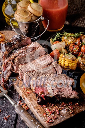 Grilled steak sliced on a cutting board. Entrecote with vegetables on a wooden background. Grilled steak sliced on a cutting board. Entrecote with vegetables on a wooden background.