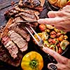 Grilled steak sliced on a cutting board. Entrecote with vegetables on a wooden background. Woman slicing a grilled beef stead.