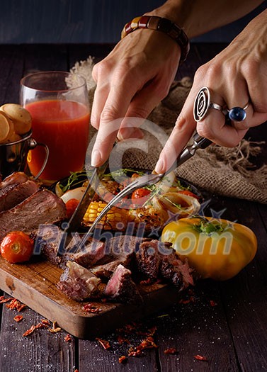 Grilled steak sliced on a cutting board. Entrecote with vegetables on a wooden background. Woman slicing a grilled beef stead. Grilled steak sliced on a cutting board. Entrecote with vegetables on a wooden background. Woman slicing a grilled beef stead.