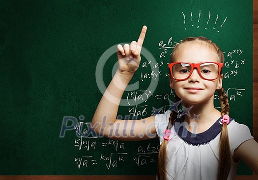 Cute school girl in glasses standing at blackboard
