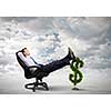 Young confident businessman sitting in chair with legs on dollar sign
