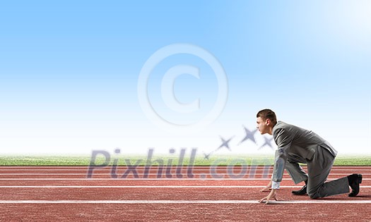 Side view of young businessman in start position on track Side view of young businessman in start position on track