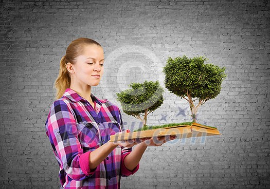 Young woman in casual holding opened book with green tree Young woman in casual holding opened book with green tree