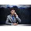 Young frustrated businessman under rain talking on mobile phone