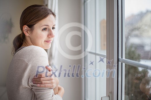 Woman looking from a window of her house on a cold and snowy winter day