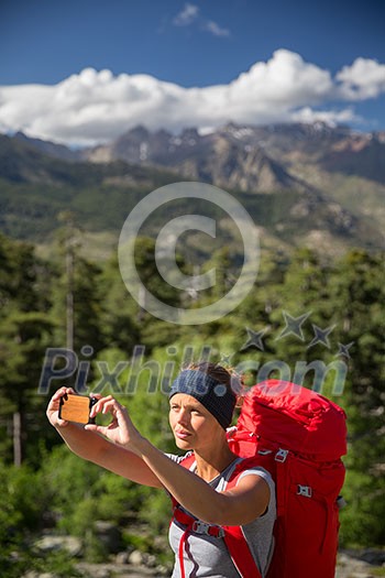 Pretty, young woman hiker taking a selfie photo with her smart phone in high mountains