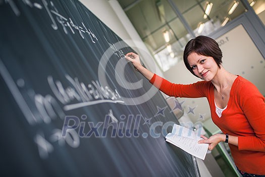 Pretty, young college student writing on the chalkboard/blackboard during a math class (color toned image)