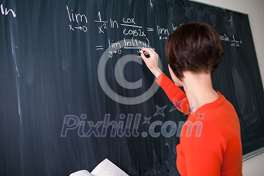 Pretty, young college student writing on the chalkboard/blackboard during a math class (color toned image)