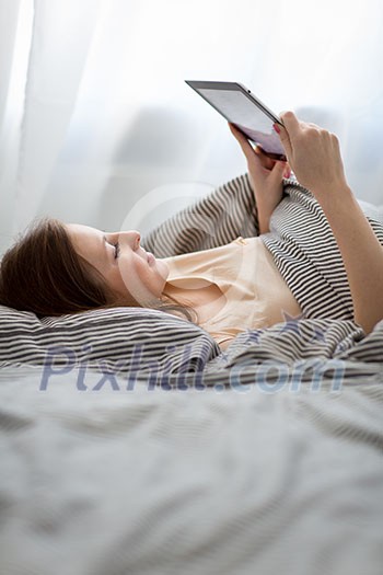 Young woman using her tablet computer in her bed (color toned image; shallow DOF)