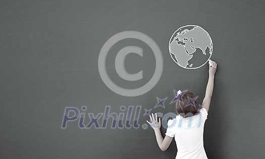 Cute little girl standing with back and drawing planet on blackboard