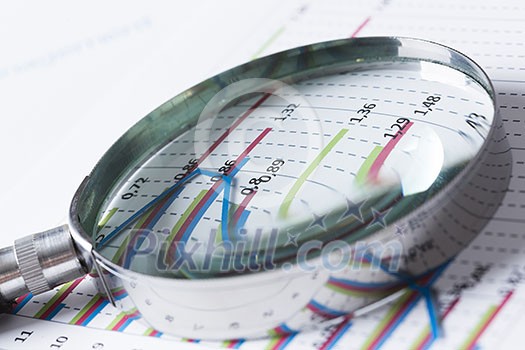 Magnifing glass and documents with analytics data lying on table