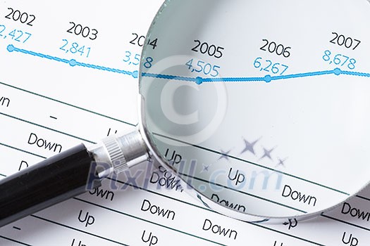 Magnifing glass and documents with analytics data lying on table