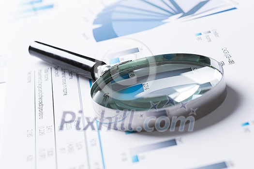 Magnifing glass and documents with analytics data lying on table