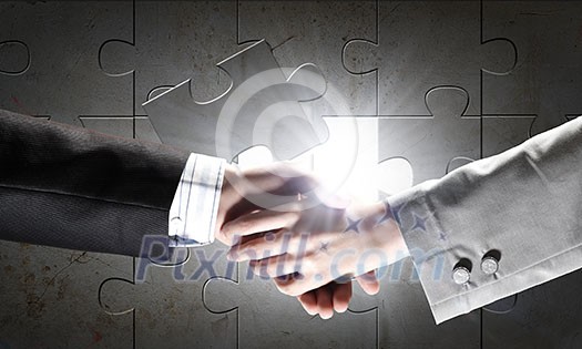Close up of business handshake with puzzle elements at background