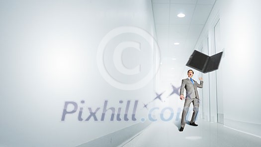 Angry young businessman in rage throwing laptop