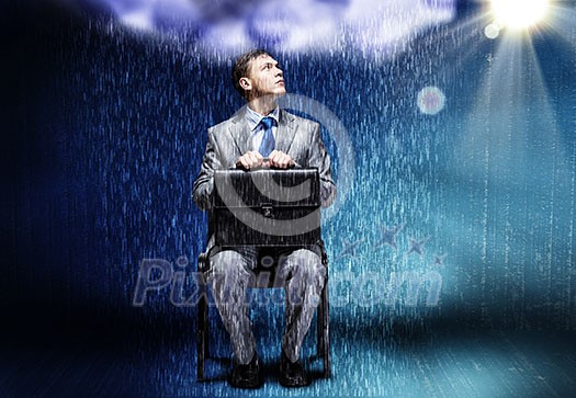 Young businessman under rain sitting on chain Young businessman under rain sitting on chain