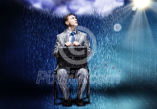 Young businessman under rain sitting on chain