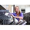 Pretty, young woman in her modern and well equiped kitchen putting cups into the dishwasher - an appliance that helps her keep the home tidy