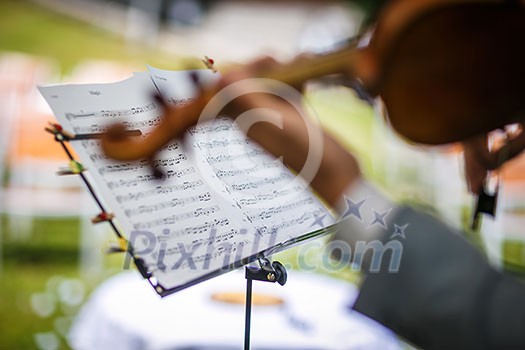 Male violinist playing his instrument and reading a music sheet during an outdoor summer wedding ceremony (shallow DOF; color toned image) Male violinist playing his instrument and reading a music sheet during an outdoor summer wedding ceremony (shallow DOF; color toned image)