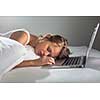 Pretty young woman falling asleep while working on her laptop in bed (shallow DOF; color toned image)