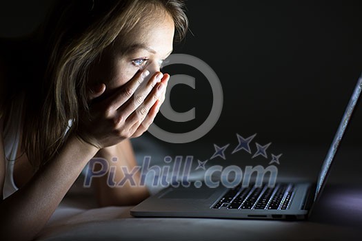 Pretty young woman watching something awful/sad on her laptop in bed