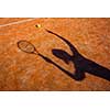 shadow of a tennis player in action on a tennis court (conceptual image with a tennis ball lying on the court and the shadow of the player positioned in a way he seems to be playing it)