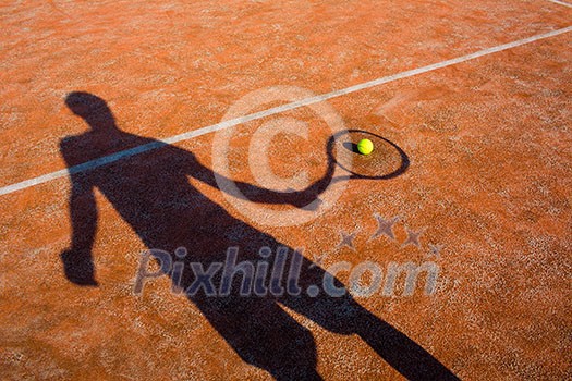 shadow of a tennis player in action on a tennis court (conceptual image with a tennis ball lying on the court and the shadow of the player positioned in a way he seems to be playing it)