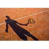 shadow of a tennis player in action on a tennis court (conceptual image with a tennis ball lying on the court and the shadow of the player positioned in a way he seems to be playing it)