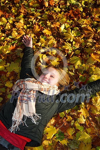 Beautiful teenage girl lying on fallen leaves in autumn park