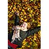 Beautiful teenage girl lying on fallen leaves in autumn park