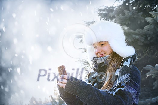 Portrait of teenage girl holding mobile phone outside in winter
