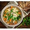 Chicken rice soup with vegetables in bowl and bread from above closeup