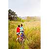 Two girls walking bicycles through rural field in summer