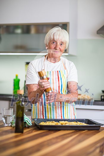 Senior woman cooking in the kitchen - eating and cooking healthy for her family; putting some potates in the oven, enjoying active retirement (shallow DOF; color toned image)