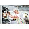 Senior woman cooking in the kitchen - eating and cooking healthy for her family; putting some potates in the oven, enjoying active retirement (shallow DOF; color toned image)