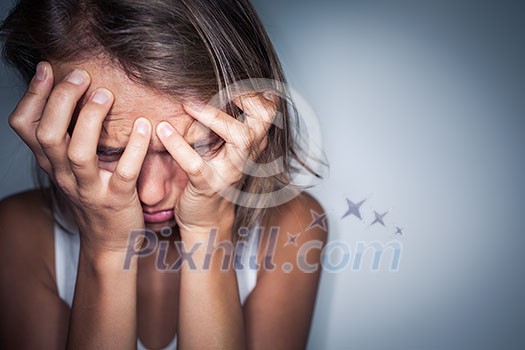 Young woman suffering from a severe depression, anxiety/sudden fear (very harsh lighting is used on this shot to underline/convey the gloomy mood of the scene; color toned image)
