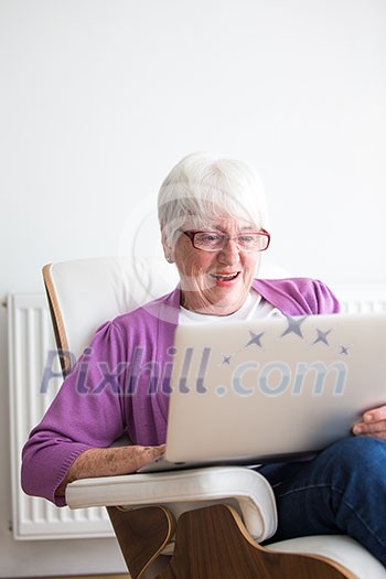 Portrait of a senior woman at home - Laughing at something on her laptop computer, sitting in her favorite chair, enjoying retirement