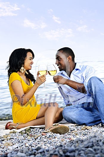 Young romantic couple celebrating with wine at the beach looking at each other