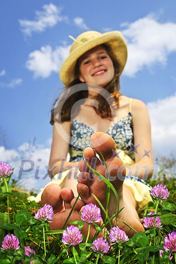 Young teenage girl sitting on summer meadow amid wildflowers in straw hat