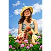 Young teenage girl sitting on summer meadow amid wildflowers in straw hat
