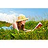 Young teenage girl reading book in summer meadow with straw hat