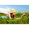 Young teenage girl reading book in summer meadow with straw hat