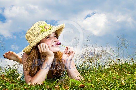 Young teenage girl laying in summer meadow resting chin on hand smelling flower