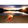 Sun setting over tranquil lake with canoe on beach