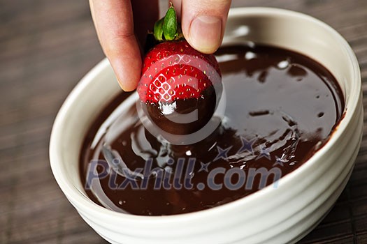 Hand dipping fresh strawberry in melted chocolate