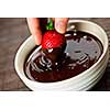 Hand dipping fresh strawberry in melted chocolate
